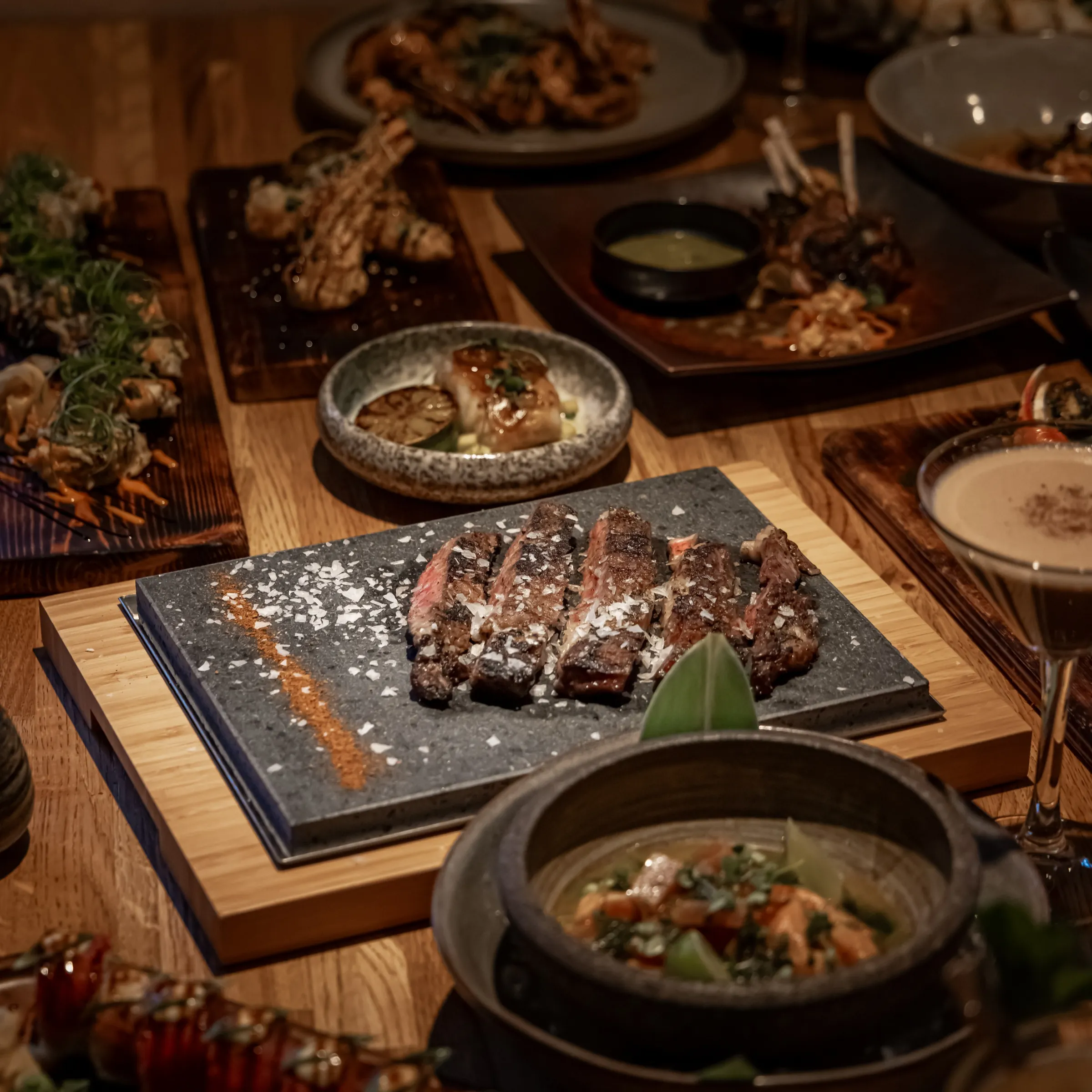 Plates to share: steak on a stone slab, small dishes and a cocktail